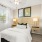 Cozy bedroom with a neatly made bed, modern wall-mounted nightstands, decorative pillows, and large windows providing natural light