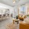 Bright and modern open-concept living room and kitchen with yellow sofas, a wooden coffee table, barstool seating at the kitchen island, and large windows